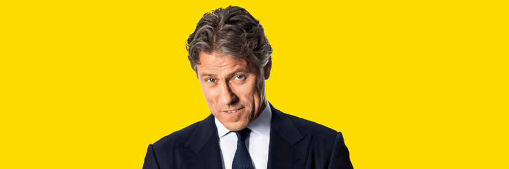 John Bishop standing with a yellow background.